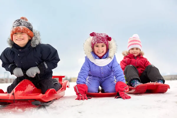Niños pequeños felices deslizándose hacia abajo en trineos en invierno —  Fotos de Stock