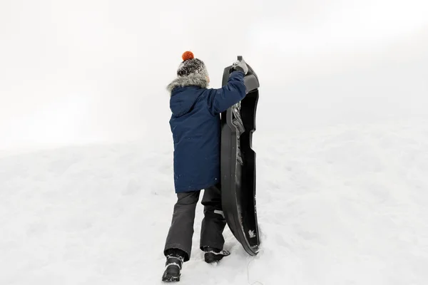 Jongetje met slee sneeuw heuvel klimmen in de winter — Stockfoto