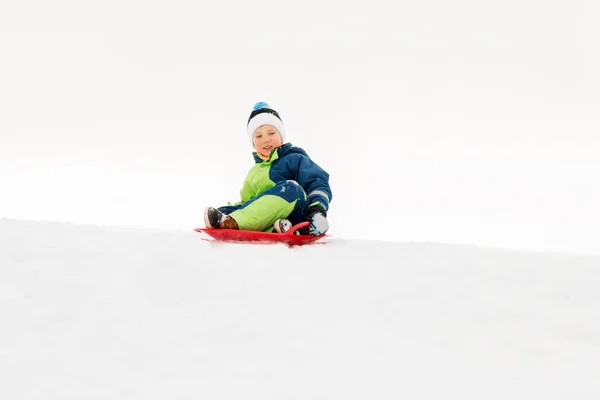 Menino feliz deslizando no trenó colina de neve no inverno — Fotografia de Stock