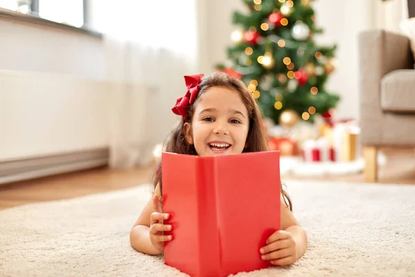 Glad tjej läser bok hemma på jul — Stockfoto