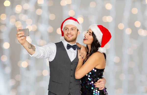 Pareja en santa sombreros tomando selfie en navidad — Foto de Stock