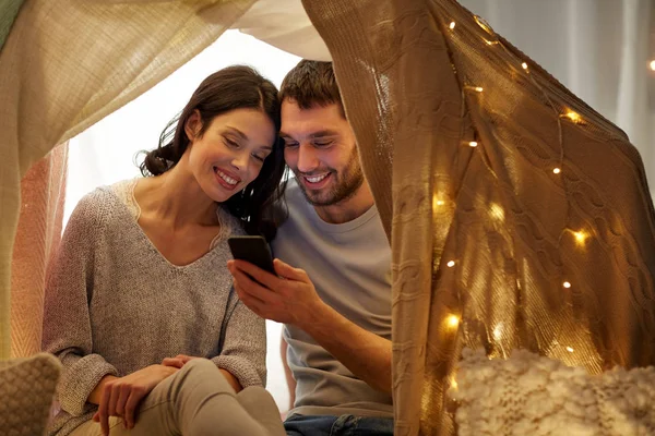 Šťastný pár se smartphone v děti stanu doma — Stock fotografie