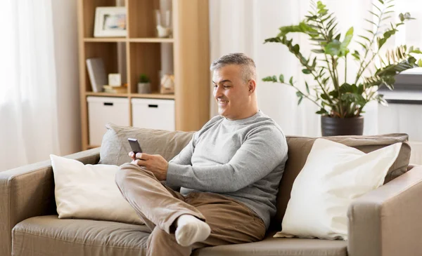 智能手机坐在家里的沙发上的男人 — 图库照片