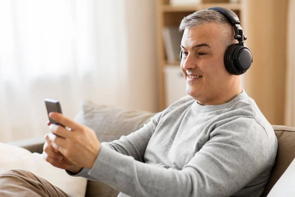 Homem com smartphone e fones de ouvido em casa — Fotografia de Stock
