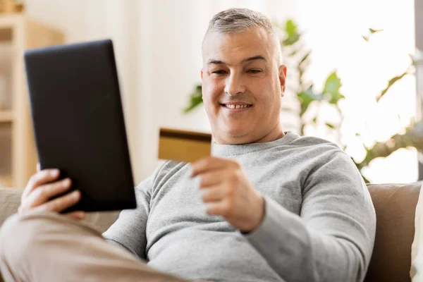 Hombre con tablet PC y tarjeta de crédito en el sofá en casa —  Fotos de Stock