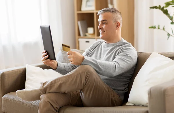 Άνθρωπος με pc ταμπλετών και την πιστωτική κάρτα στον καναπέ στο σπίτι — Φωτογραφία Αρχείου