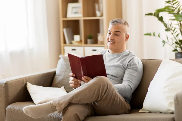 Мужчина сидит на диване и читает книгу дома — стоковое фото