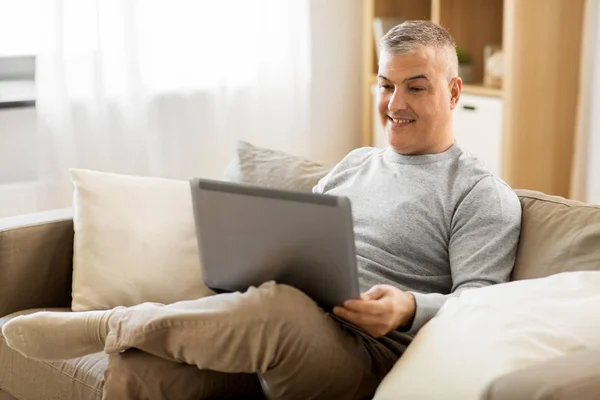 Homme avec ordinateur portable assis sur le canapé à la maison — Photo
