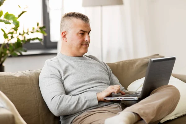 Человек с ноутбуком компьютер сидит на диване дома — стоковое фото