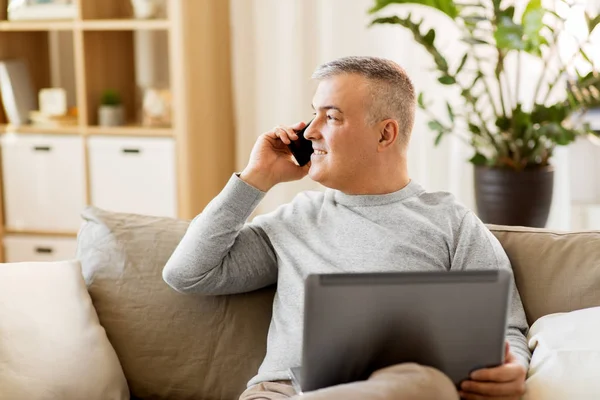 Hombre con el ordenador portátil llamando en el teléfono inteligente en casa —  Fotos de Stock