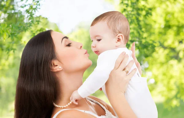 Mother kissing baby over green natural background — Stock Photo, Image