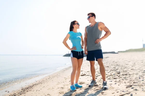 Casal feliz em roupas esportivas e tons na praia — Fotografia de Stock