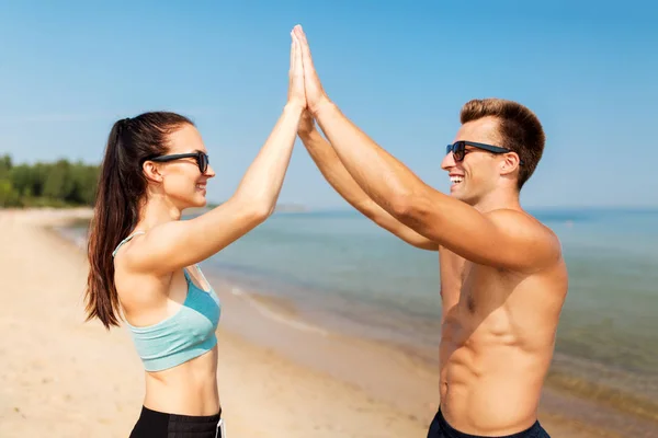 Gelukkige paar in sport kleding en tinten op strand — Stockfoto