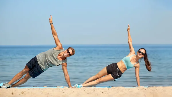 Casal fazendo exercício de prancha lateral na praia de verão — Fotografia de Stock