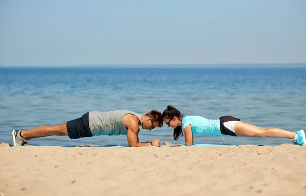 Pareja haciendo ejercicio de tablón en la playa de verano —  Fotos de Stock