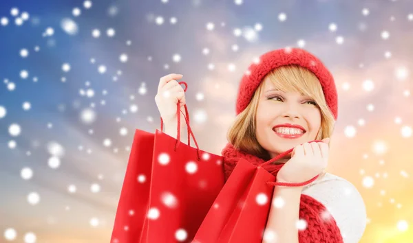 Kar arka plan üzerinde kırmızı alışveriş torbaları kadınla — Stok fotoğraf