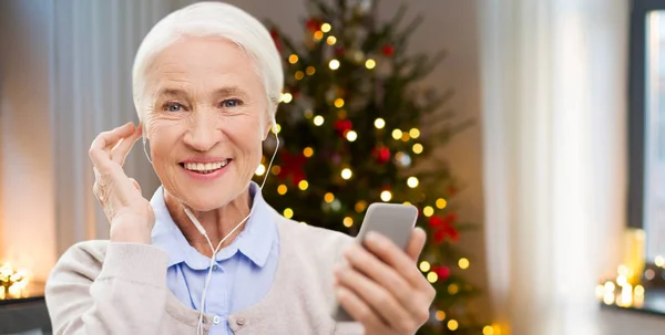 Senior vrouw met oortelefoons en telefoon op Kerstmis — Stockfoto