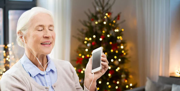 Starší žena s smartphone a sluchátka doma — Stock fotografie