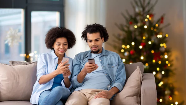 互联网和通信的概念 愉快的非洲美国人夫妇与智能手机在家里圣诞树灯背景 — 图库照片