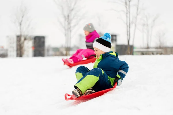 Crianças deslizando em trenós para baixo colina de neve no inverno — Fotografia de Stock