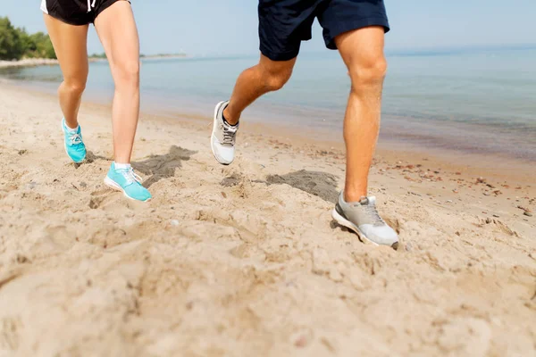 Piernas de deportistas en zapatillas de deporte a lo largo de la playa — Foto de Stock