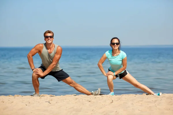 Sorridente coppia stretching gambe su spiaggia — Foto Stock