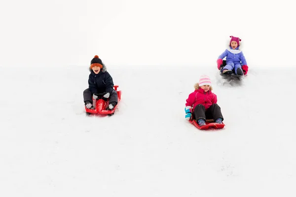 Crianças deslizando em trenós para baixo colina de neve no inverno — Fotografia de Stock