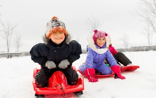 Glückliche kleine Kinder, die im Winter auf Schlitten nach unten rutschen — Stockfoto