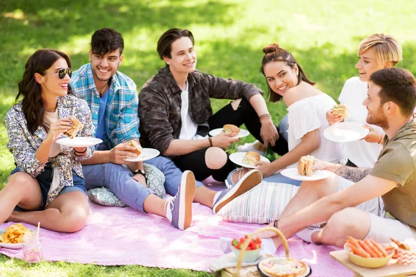 Amici felici mangiare panini al picnic estivo — Foto Stock