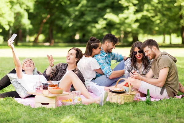 Друзі зі смартфонами на пікніку в літньому парку — стокове фото