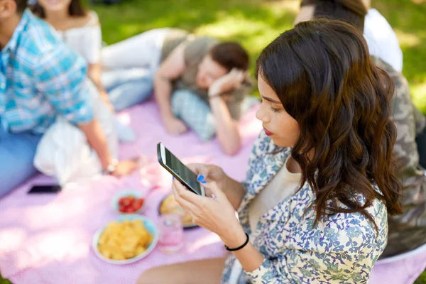 Женщина с помощью смартфона на пикнике с друзьями — стоковое фото