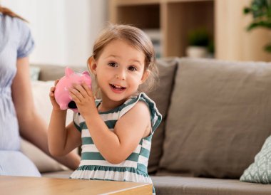 savings and finances concept - happy little girl with piggy bank at home clipart