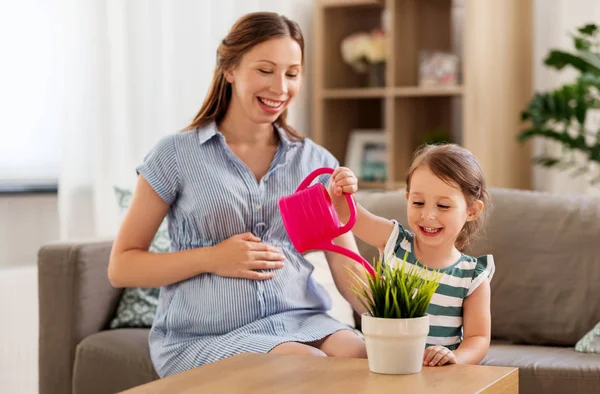 Mère enceinte et fille arrosage plante à la maison — Photo