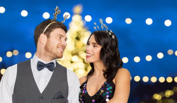 Couple with party props over christmas tree lights — Stock Photo, Image