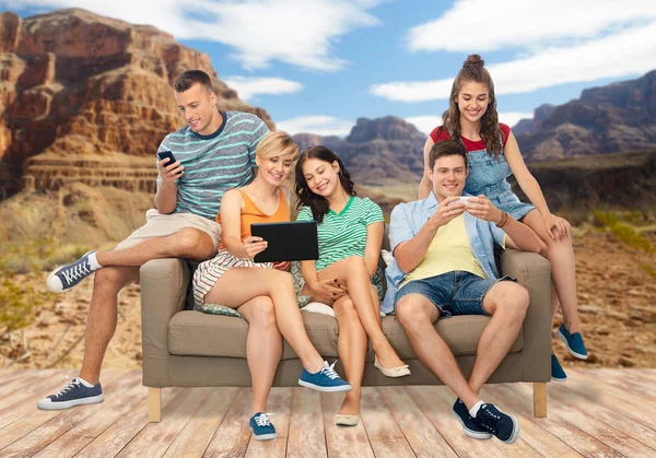 Друзья с планшетным ПК и смартфоны сидеть на диване — стоковое фото