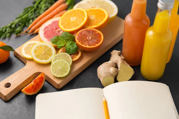 Närbild av frukter, juicer och anteckningsbok på tabell — Stockfoto