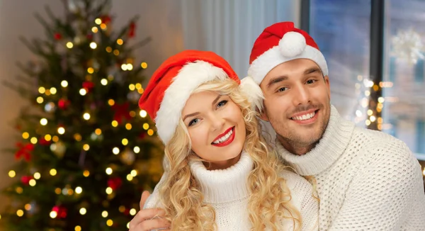 Paar in Weihnachtsmannmützen über Weihnachtsbaumbeleuchtung — Stockfoto