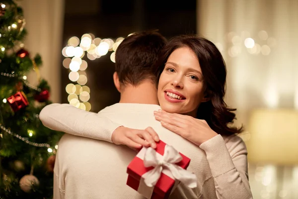 Щаслива пара з різдвяним подарунком обіймається вдома — стокове фото