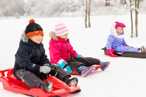 Niños pequeños felices deslizándose en trineos en invierno —  Fotos de Stock