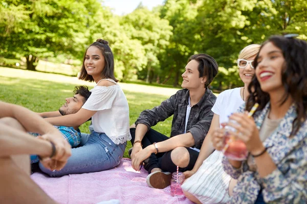 Happy friends with drinks at picnic in summer park — Stock Photo, Image