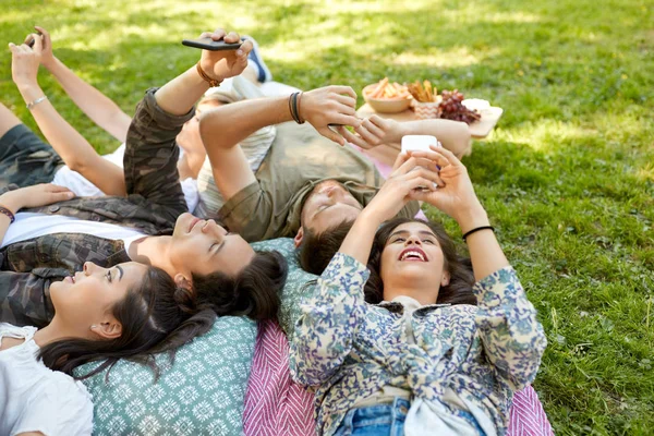 Vrienden met smartphones koelen in zomer park — Stockfoto