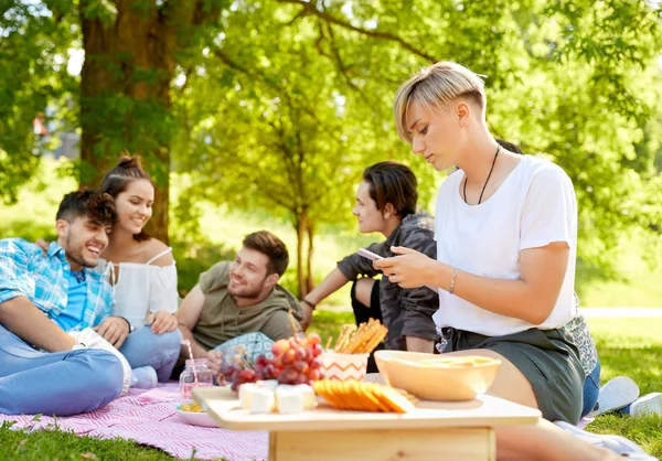 Vrouw met behulp van smartphone op picnic met vrienden — Stockfoto