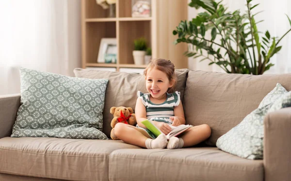 Šťastná dívka sedí na pohovce s knihou doma — Stock fotografie