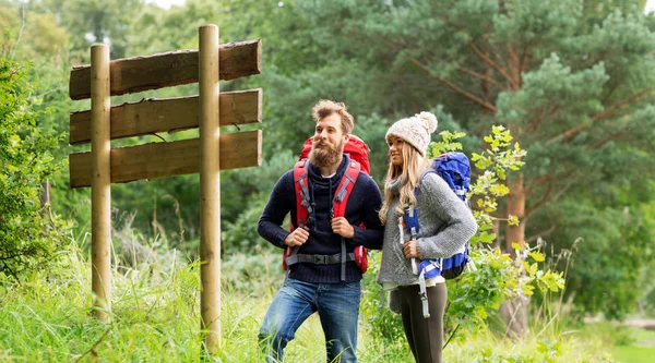 Couple of travelers with backpacks at signpost — Stock Photo, Image