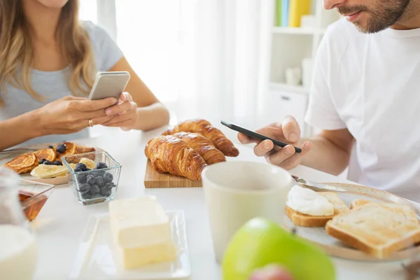 Close up of couple with smartphones at breakfast — Stock Photo, Image