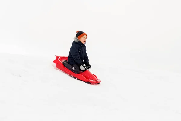 Heureux garçon glissant sur traîneau descendant neige colline en hiver — Photo