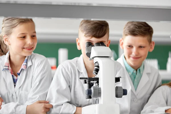 Niños o estudiantes con biología de microscopio en la escuela — Foto de Stock