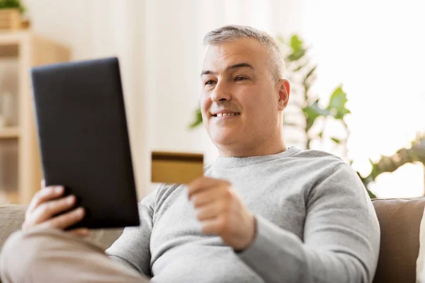 Człowiek z komputera typu tablet i karty kredytowej na kanapie w domu — Zdjęcie stockowe