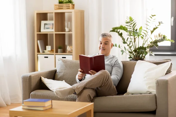 Hombre sentado en el sofá y leyendo libro en casa — Foto de Stock