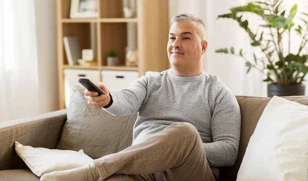 Hombre con mando a distancia viendo la televisión en casa — Foto de Stock